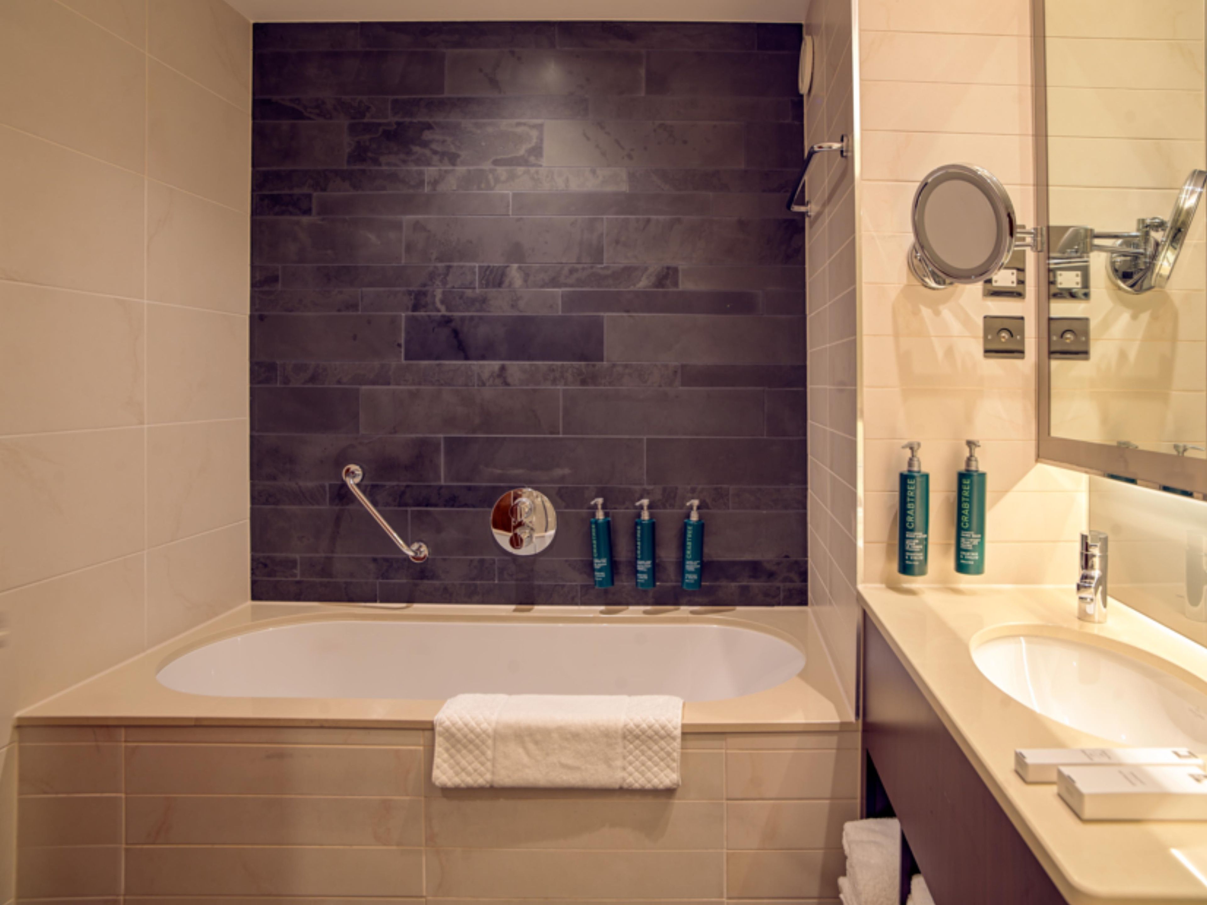 A bathroom with a bathtub, a vanity with a mirror, and toiletries on the wall.