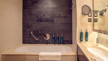 A bathroom with a bathtub, a vanity with a mirror, and toiletries on the wall.