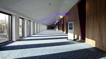 A long, narrow hallway with patterned flooring, large windows on one side, and wooden paneling on the other.