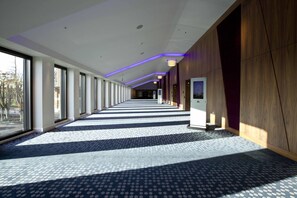 A long, narrow hallway with patterned flooring, large windows on one side, and wooden paneling on the other. - Hilton London Heathrow Airport Terminal 5 Hotel Conference Centre (Slough)