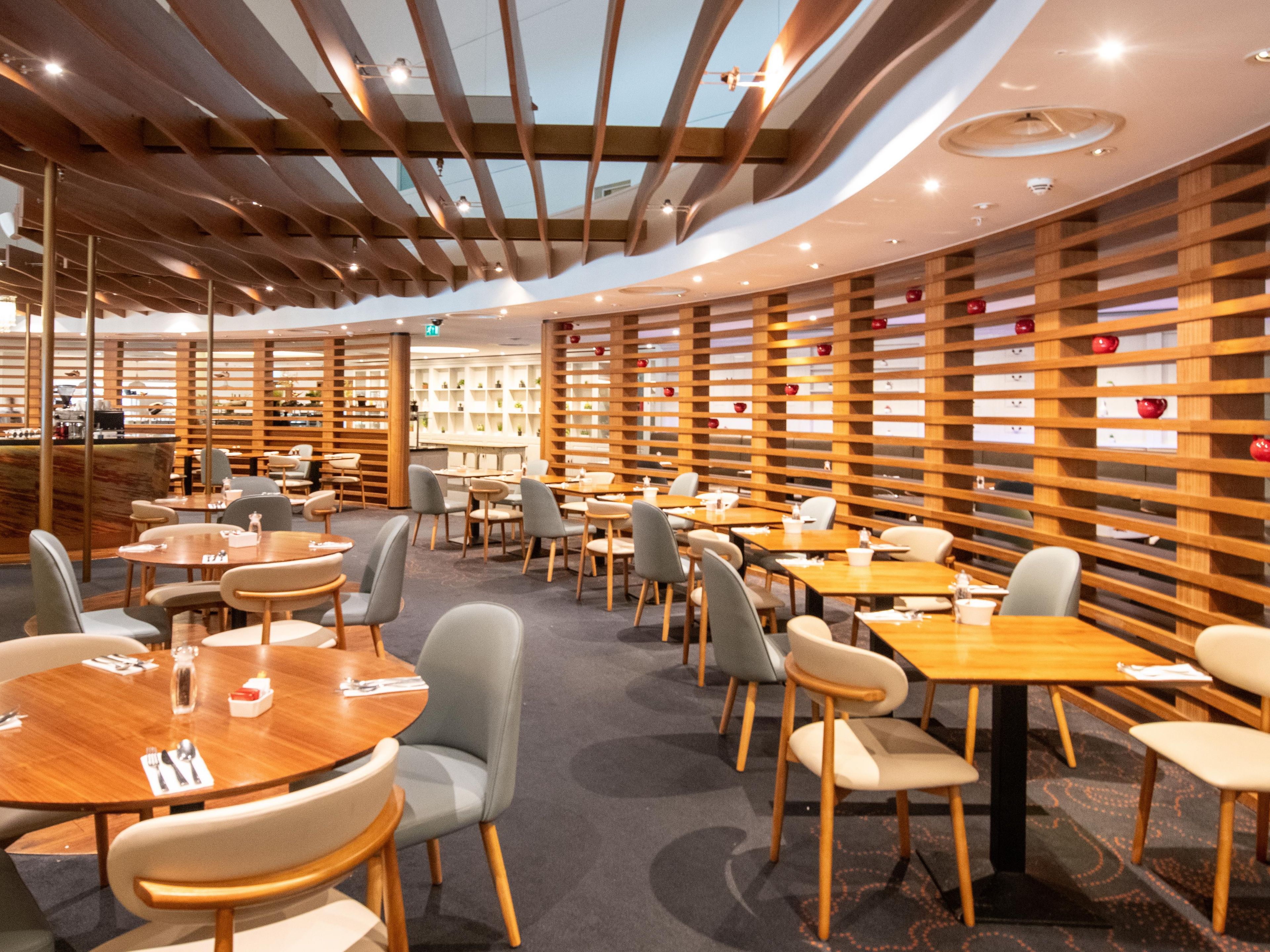 A modern restaurant with round tables and chairs, wooden slatted walls, and a ceiling with exposed beams.