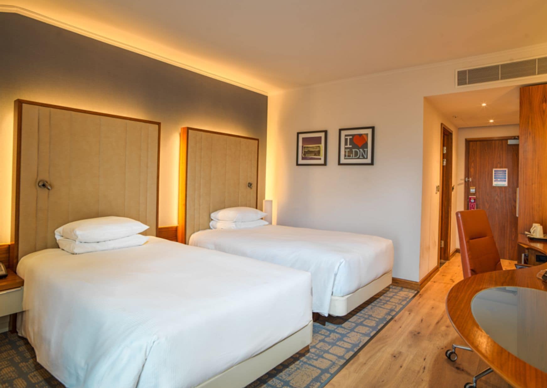 Una camera d'albergo con due letti, una scrivania in legno e una sedia.