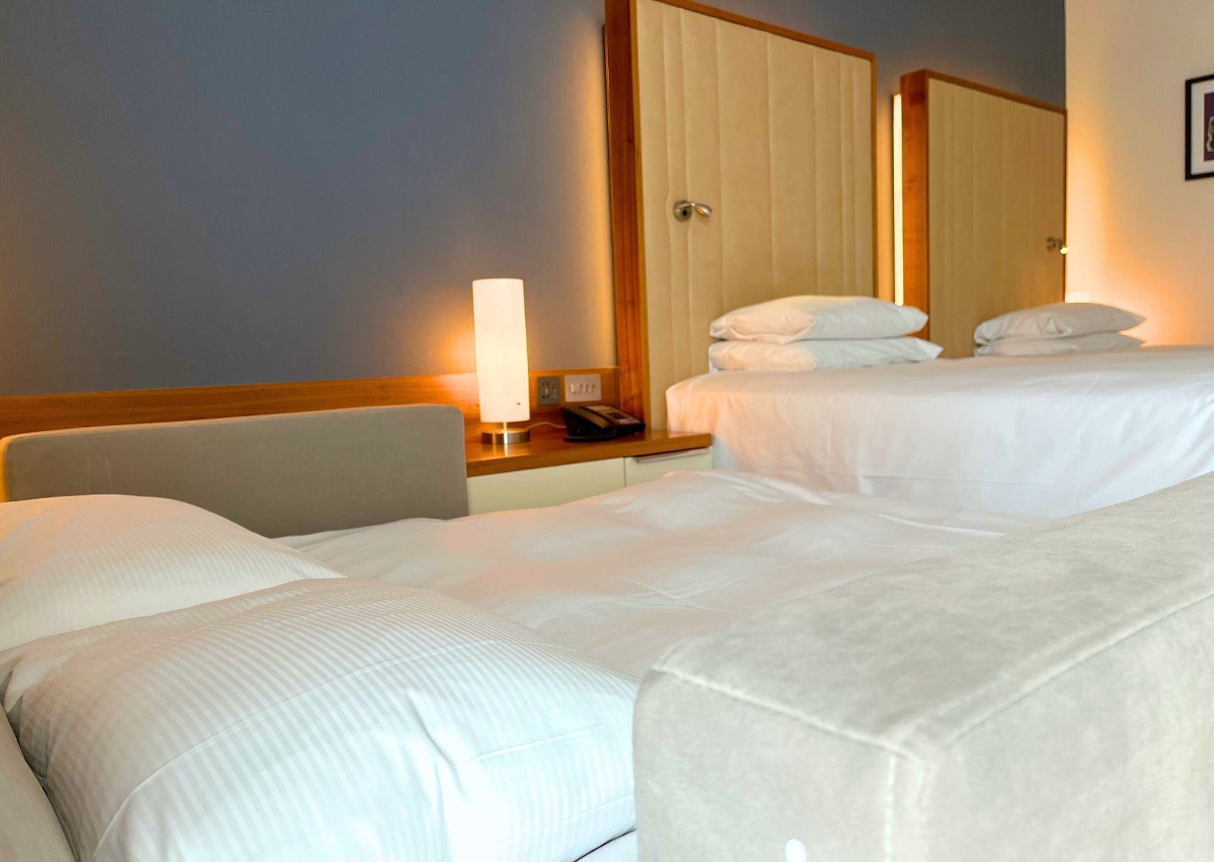 Une chambre d’hôtel avec deux lits, une table de chevet avec une lampe, un téléphone et une porte.