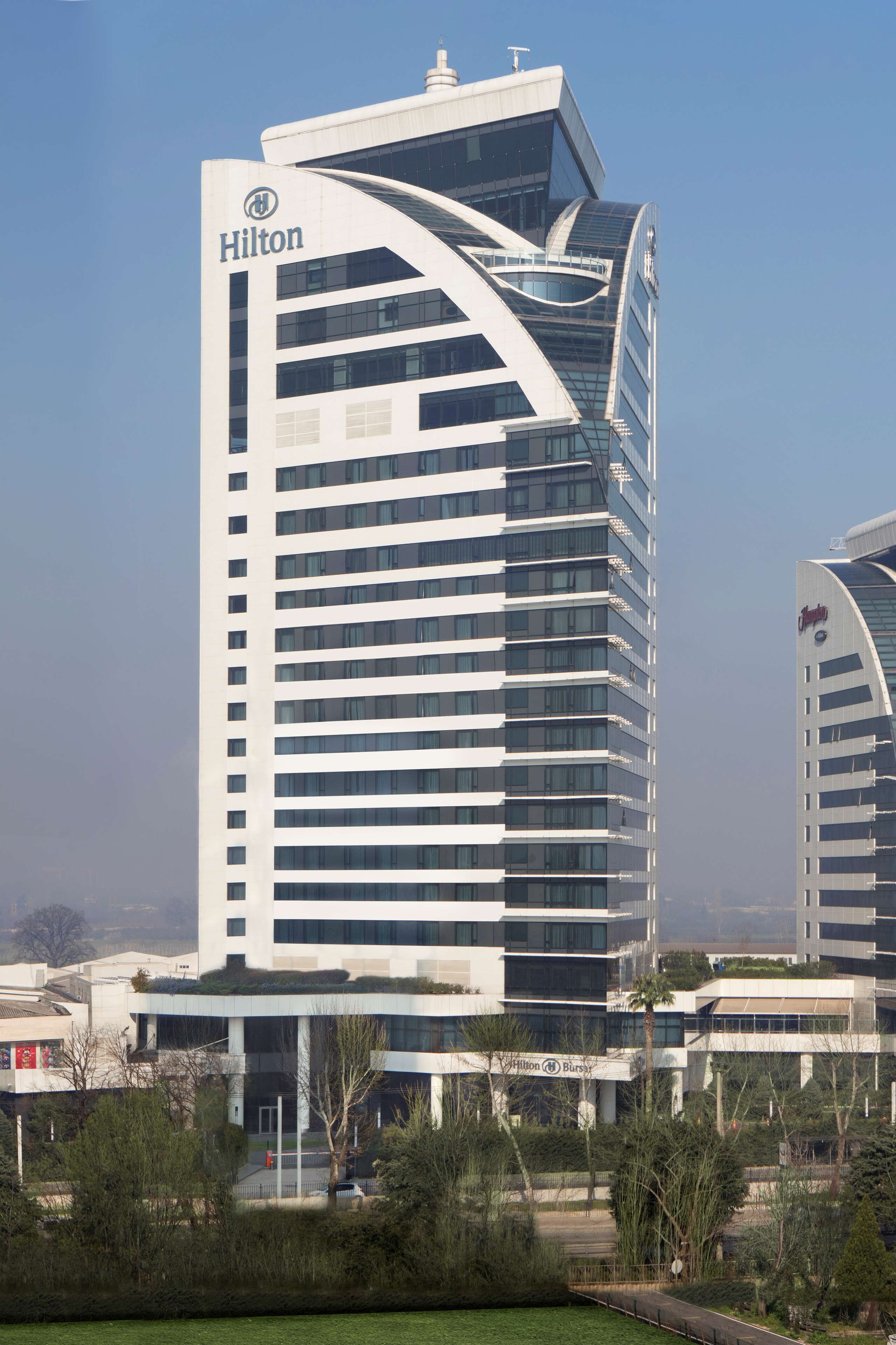 A modern Hilton hotel with a distinctive curved facade and multiple floors.
