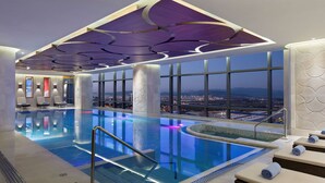 Une piscine intérieure moderne offrant une vue sur le paysage urbain, dotée de grandes fenêtres et d’un design de plafond original.