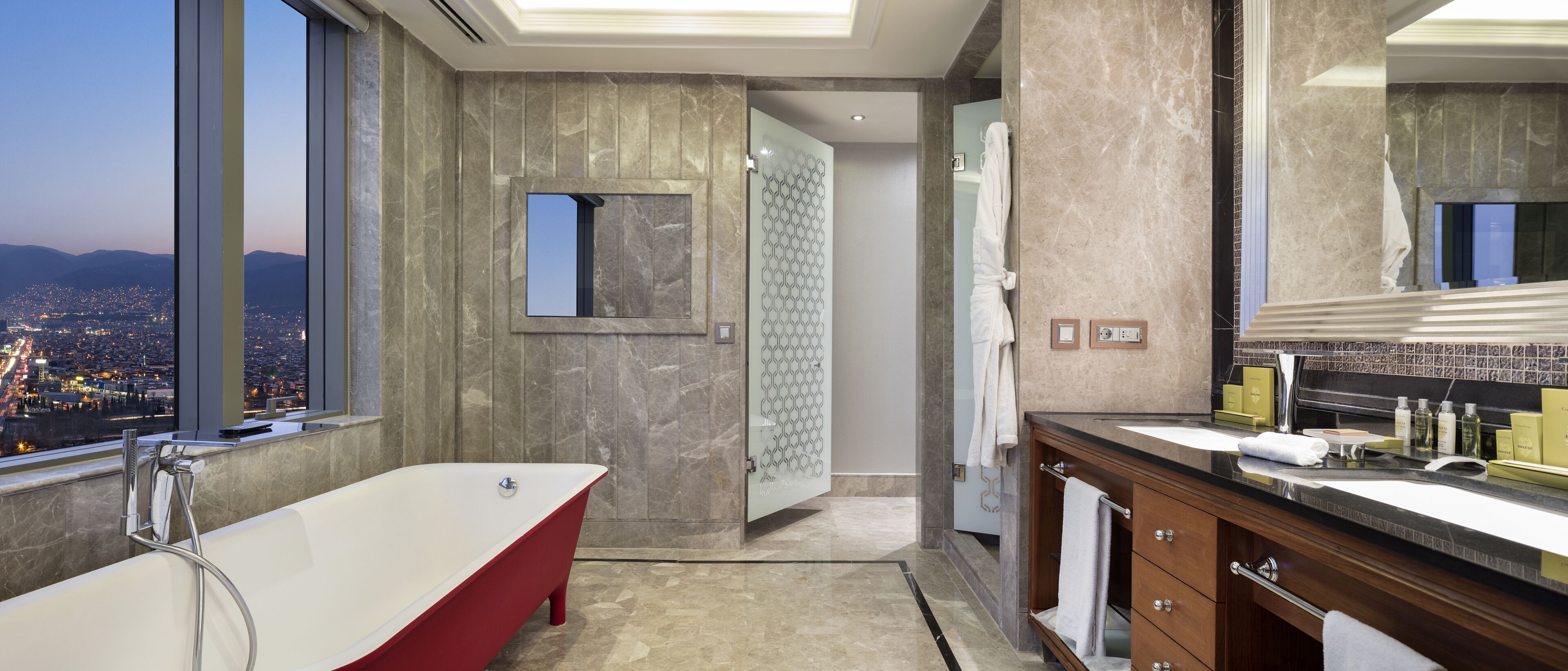 A modern bathroom with a freestanding bathtub, a vanity with a large mirror, and a view of the city through a large window.