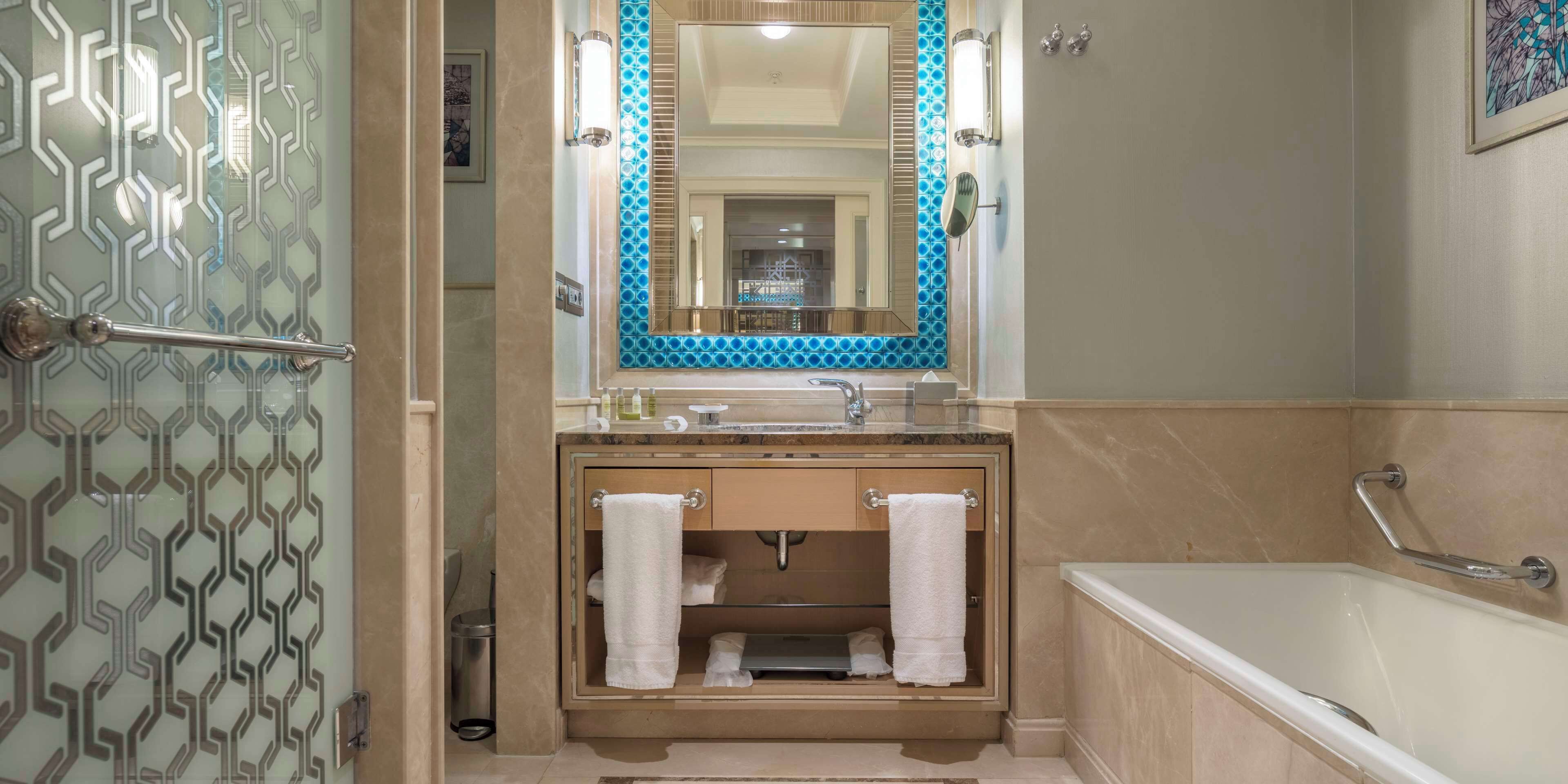 Une salle de bain avec une porte en verre, un lavabo avec un miroir, une baignoire et un porte-serviettes.