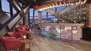 Un bar moderne avec des fauteuils en cuir rouge, un comptoir offrant une vue sur la ville et un design de plafond unique.