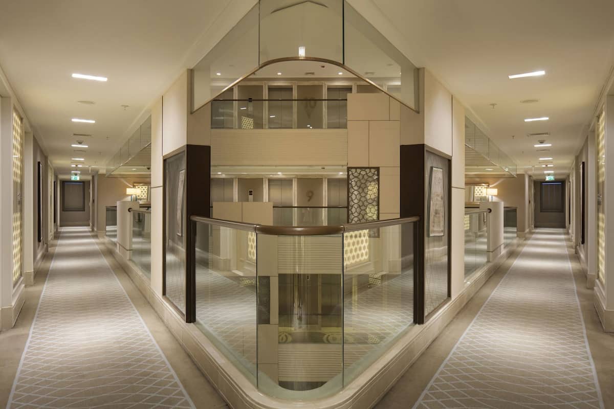 A hotel corridor with a glass railing, multiple floors, and a central elevator.