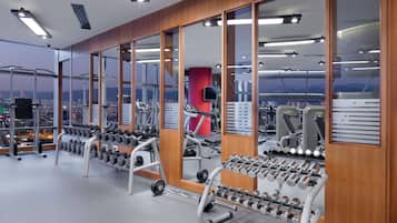 Un gimnasio con equipos de ejercicio variados, ventanas amplias y vistas a la ciudad.