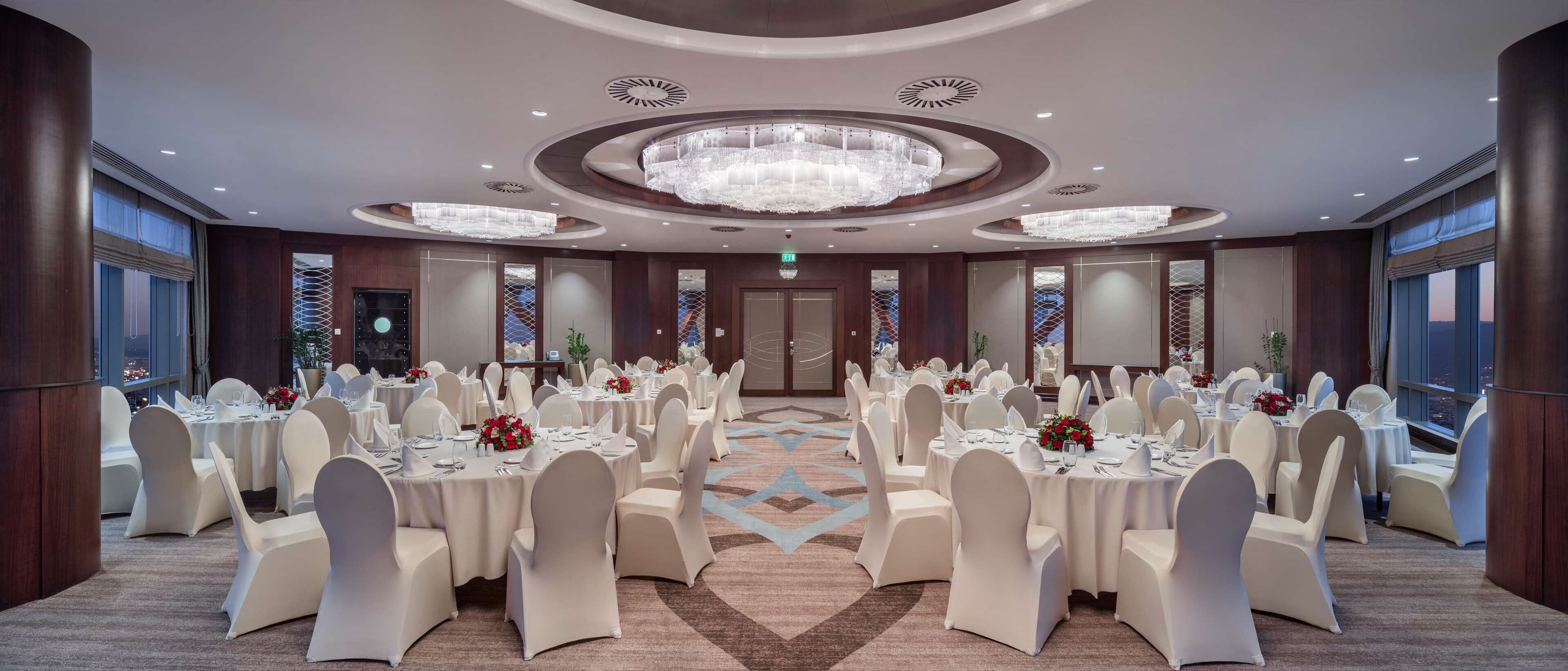 A banquet hall with round tables, white chairs, and chandeliers.