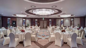 Un salón de banquetes con mesas redondas, sillas blancas y candelabros.