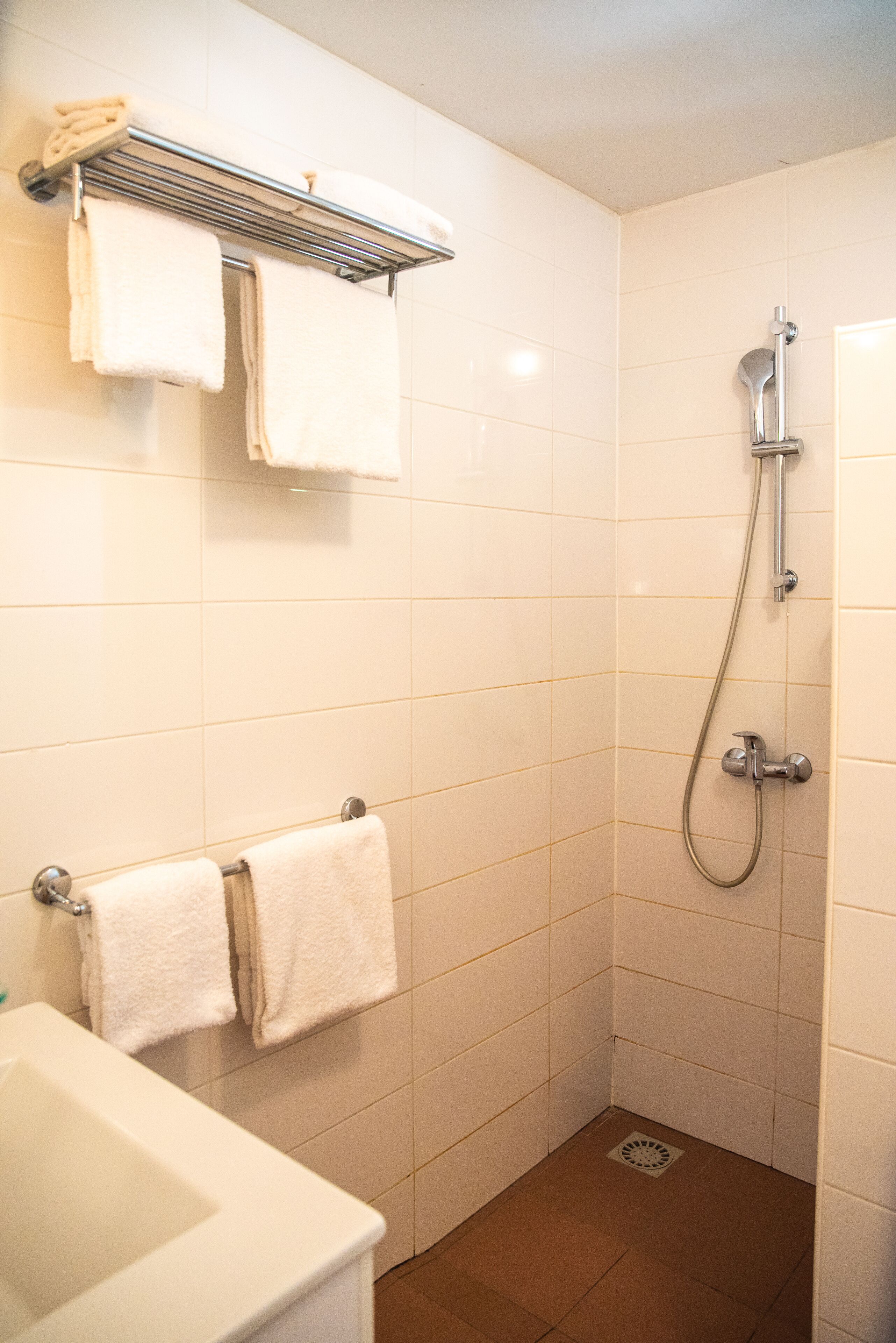Une petite salle de bain propre, avec des carreaux blancs, une douche, un porte-serviettes et un lavabo.