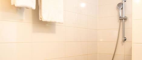Une petite salle de bain propre, avec des carreaux blancs, une douche, un porte-serviettes et un lavabo.