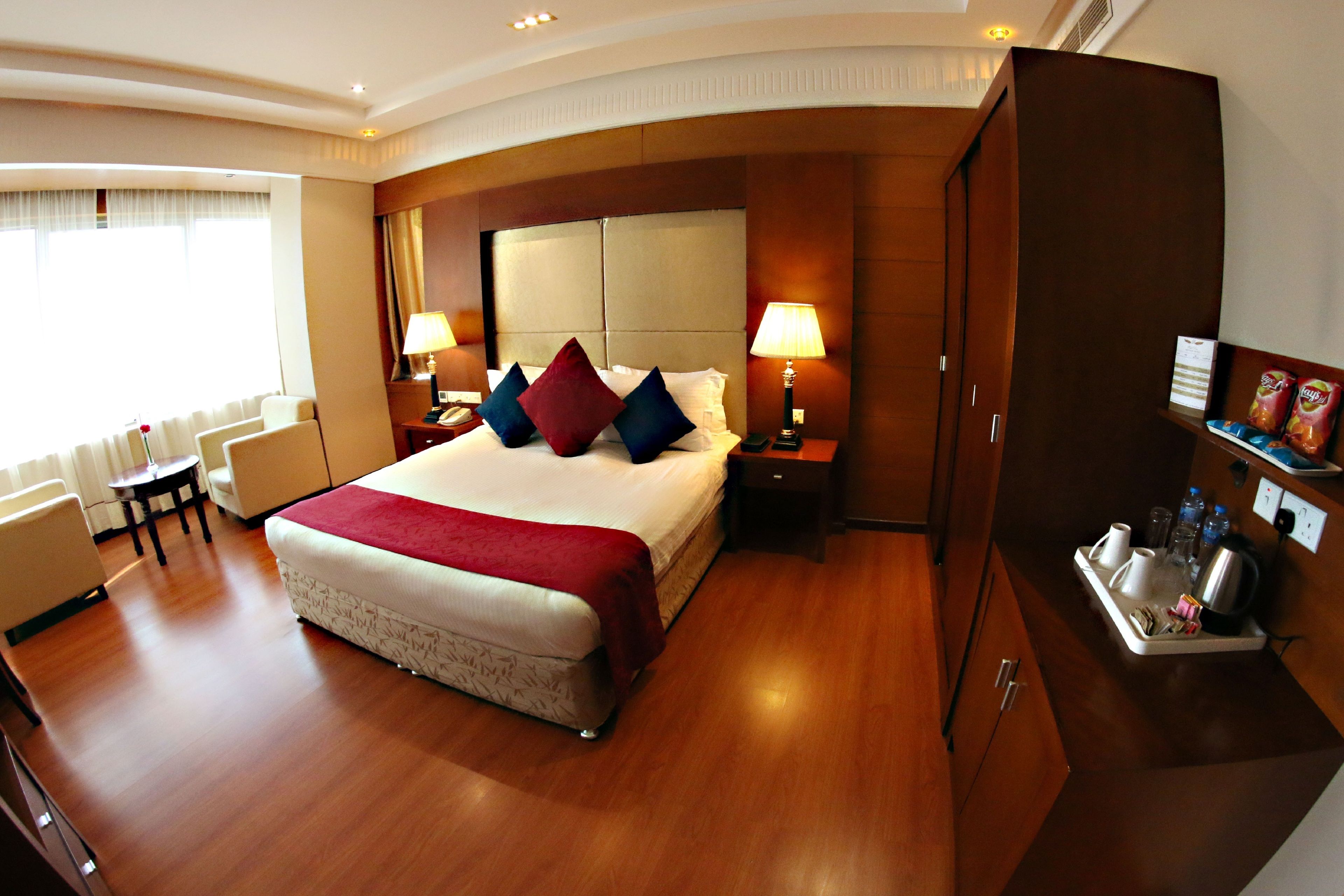 A hotel room with a large bed, two bedside tables, a desk, a chair, a wardrobe, and a tray with toiletries.