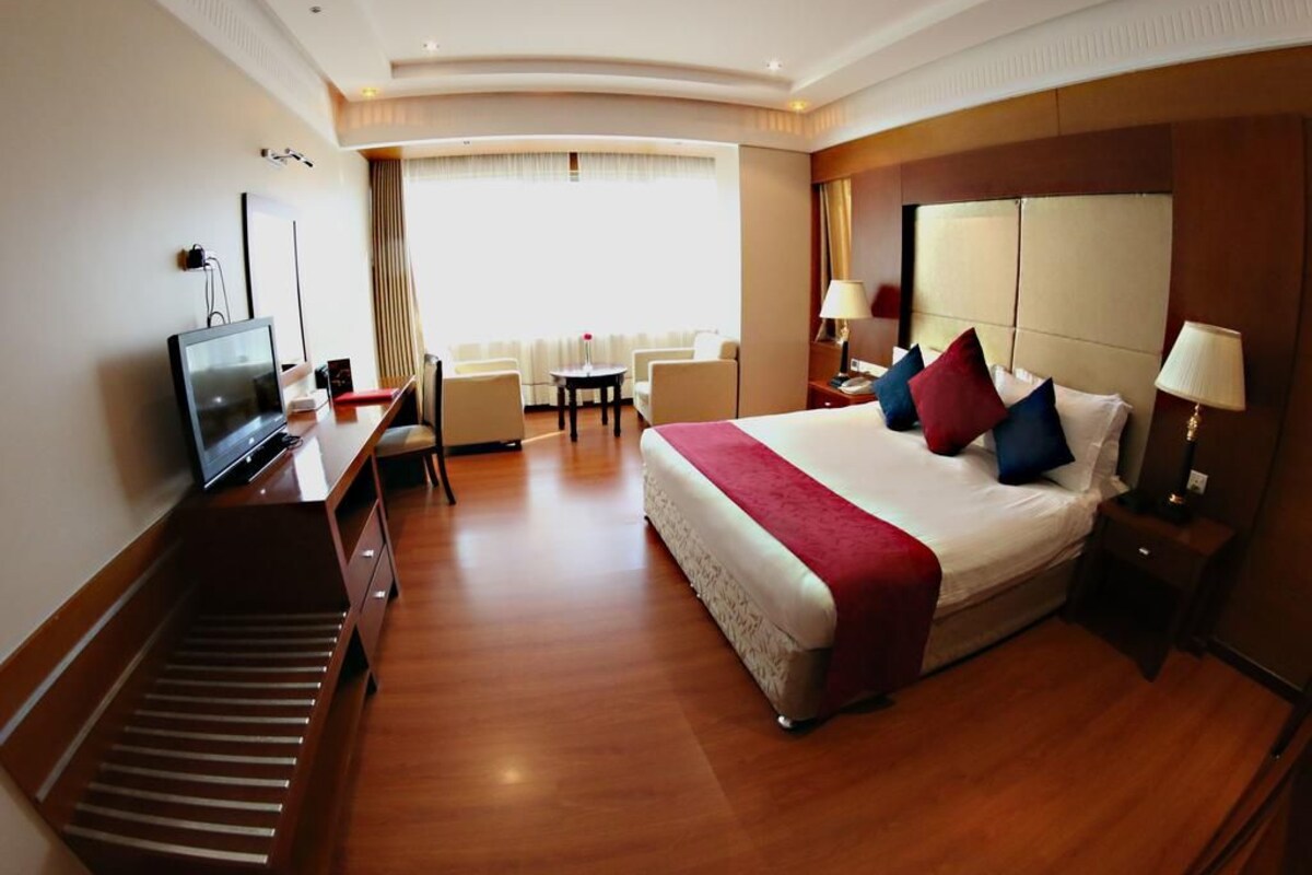A hotel room with a bed, bedside tables, a desk with a computer, a TV, and a seating area with chairs and a table.