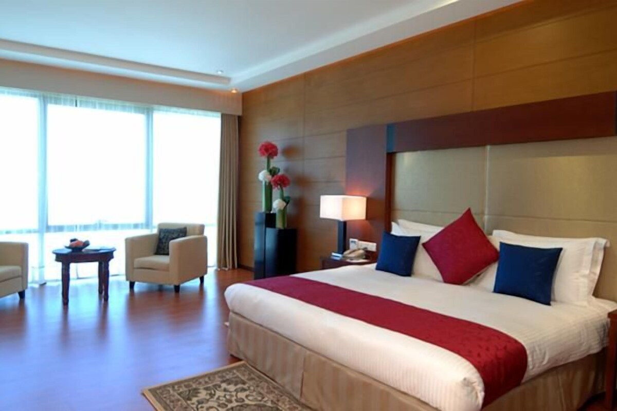 A hotel room with a large bed, two armchairs, a small table, and a vase of flowers.