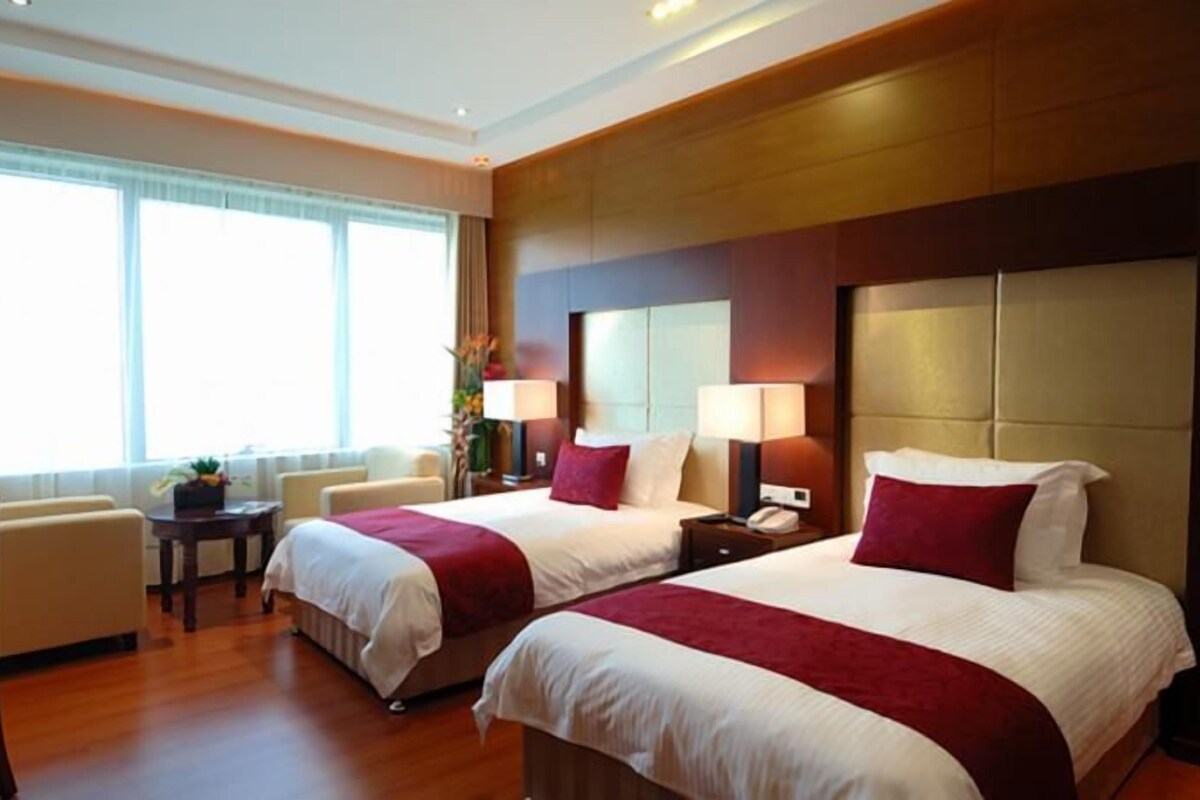 A hotel room with two beds, a sitting area with a chair, a small table, and a window with curtains.