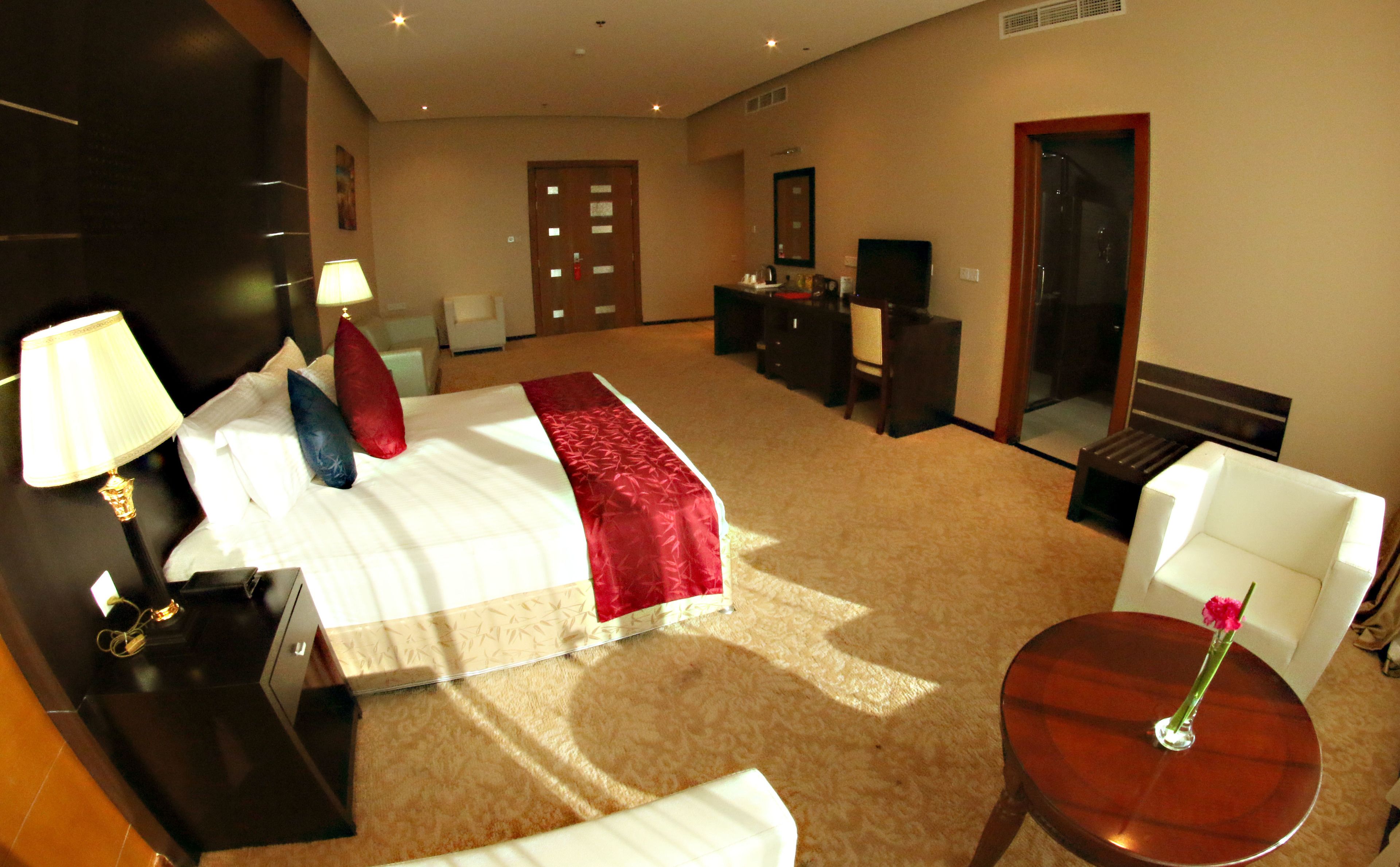 A hotel room with a bed, bedside tables, a desk, a chair, a small table with a vase, and a mirror.