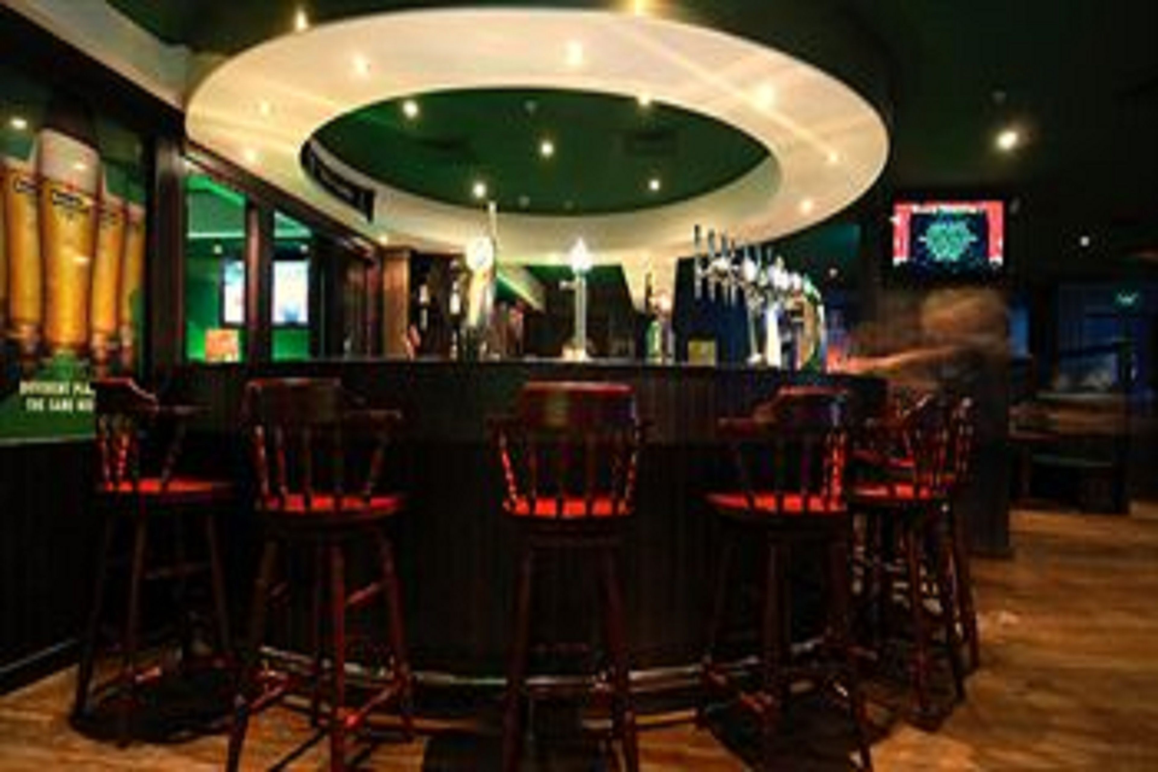 Zona de bar con mostrador circular, varios taburetes y una pantalla de televisión al fondo.