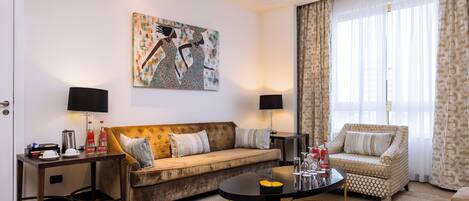 Un salón luminoso con sofá, sillones, una mesa de centro y un cuadro en la pared.