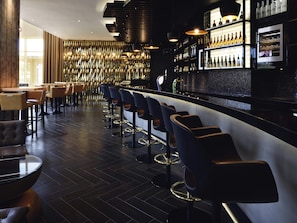 A bar area with high stools, a counter, and shelves with bottles. - Mövenpick Ambassador Hotel Accra (Accra)