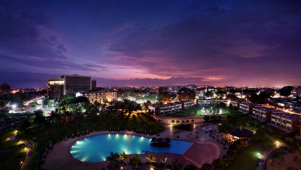 A hotel with a large swimming pool, multiple buildings, and a cityscape in the background. - Mövenpick Ambassador Hotel Accra (Accra)