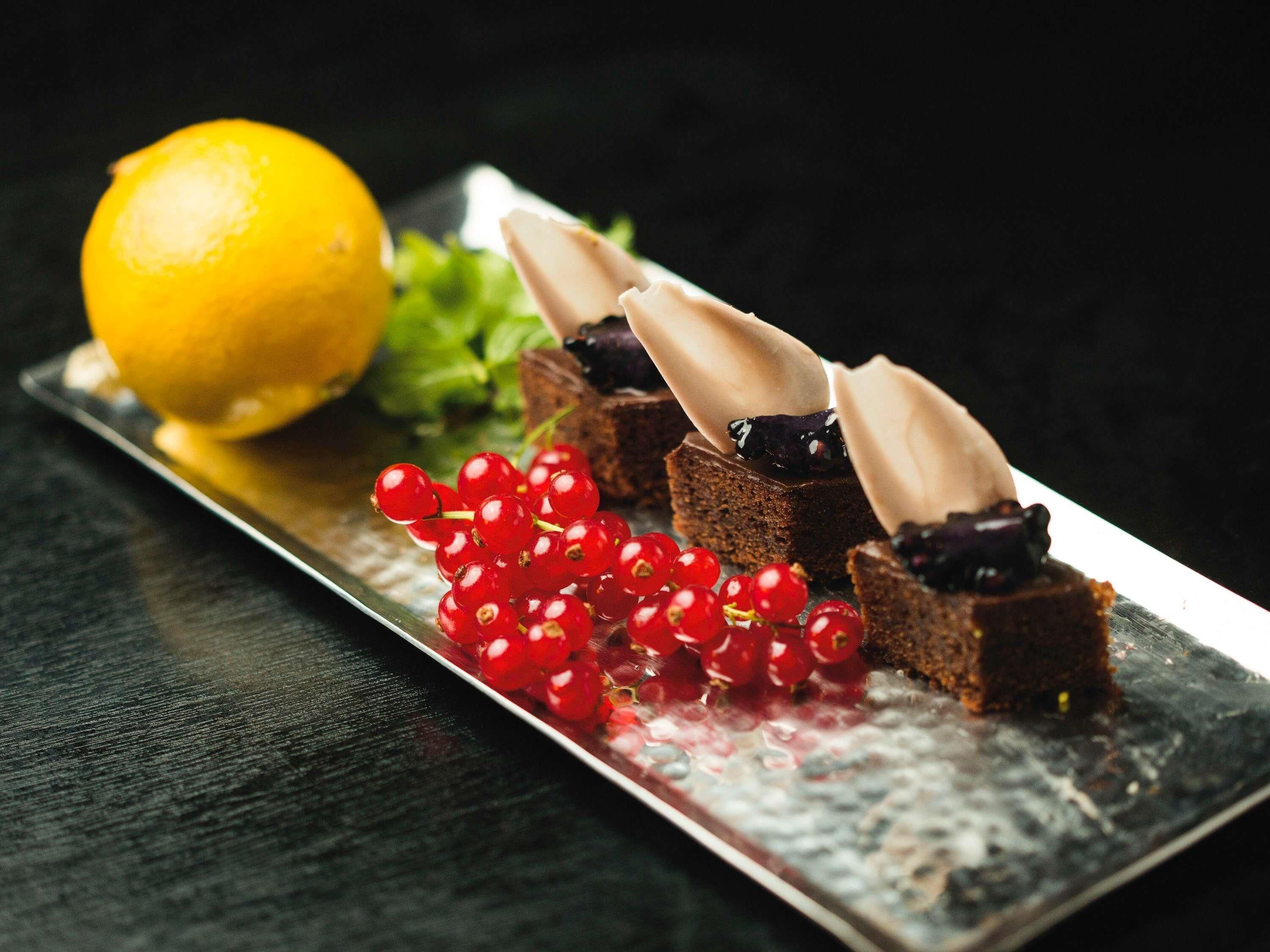 A dessert plate with chocolate pieces, red currants, and a lemon.