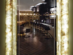 A bar area with a curved counter, multiple bar stools, and a patterned wall in the background. - Mövenpick Ambassador Hotel Accra (Accra)
