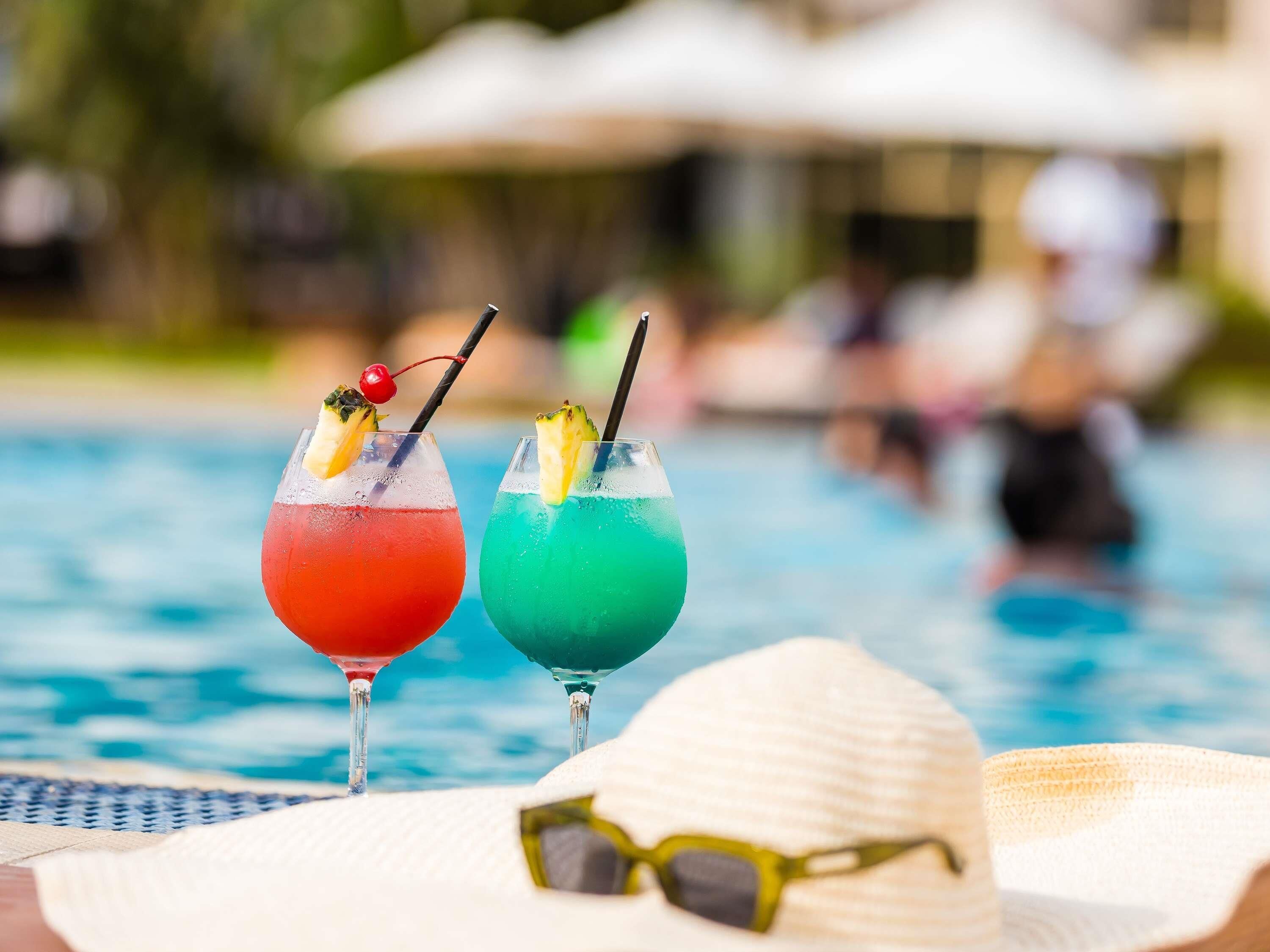 Two cocktails with fruit garnishes on a poolside table.