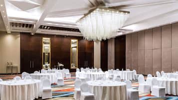 A conference room with round tables, white chairs, a chandelier, and a carpeted floor.