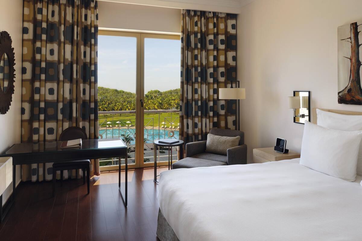 Ein Hotelzimmer mit Bett, Schreibtisch, Stuhl, Sofa und Blick auf Pool und Grünflächen.