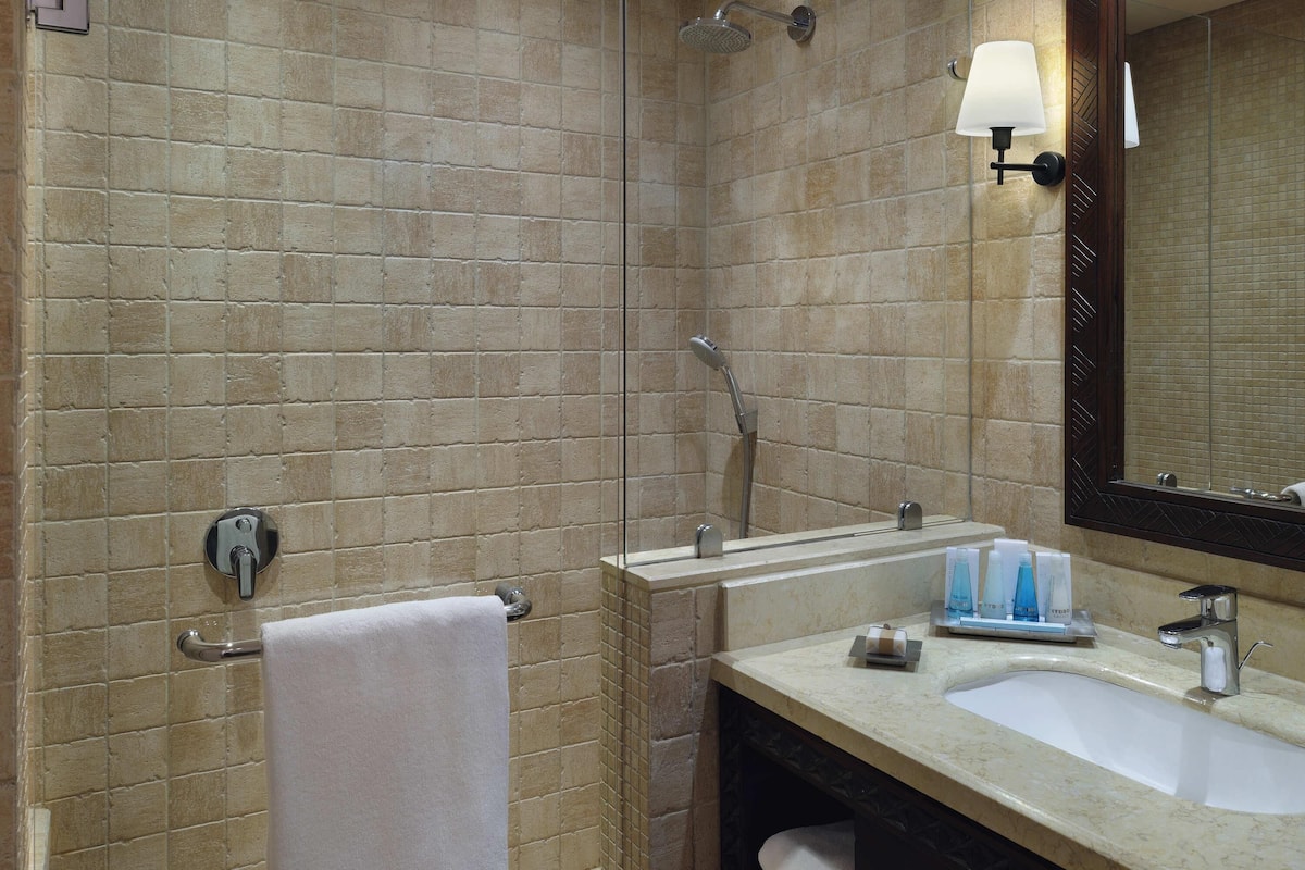 A bathroom with a sink, mirror, towel rack, and shower.