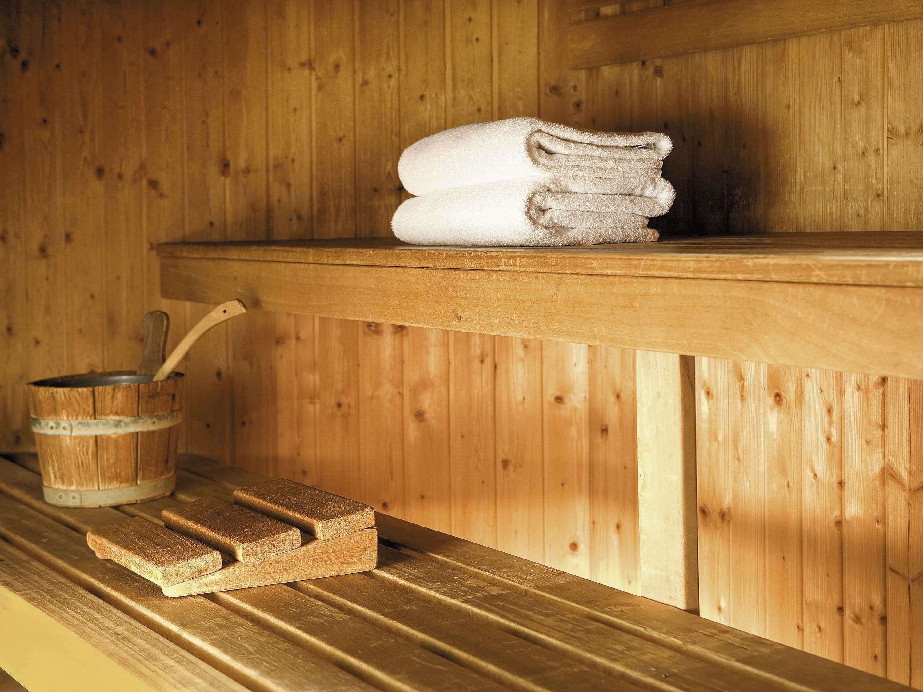 Una sauna de madera con un banco, una pila de toallas y un cubo de madera con una cuchara.