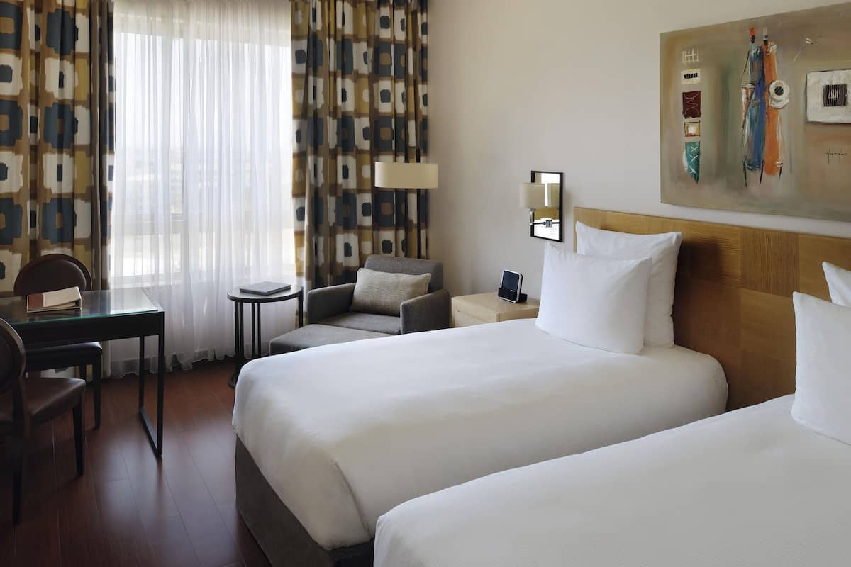 Ein Hotelzimmer mit zwei Betten, einem Schreibtisch, einem Stuhl, einem kleinen Tisch und einer Lampe.
