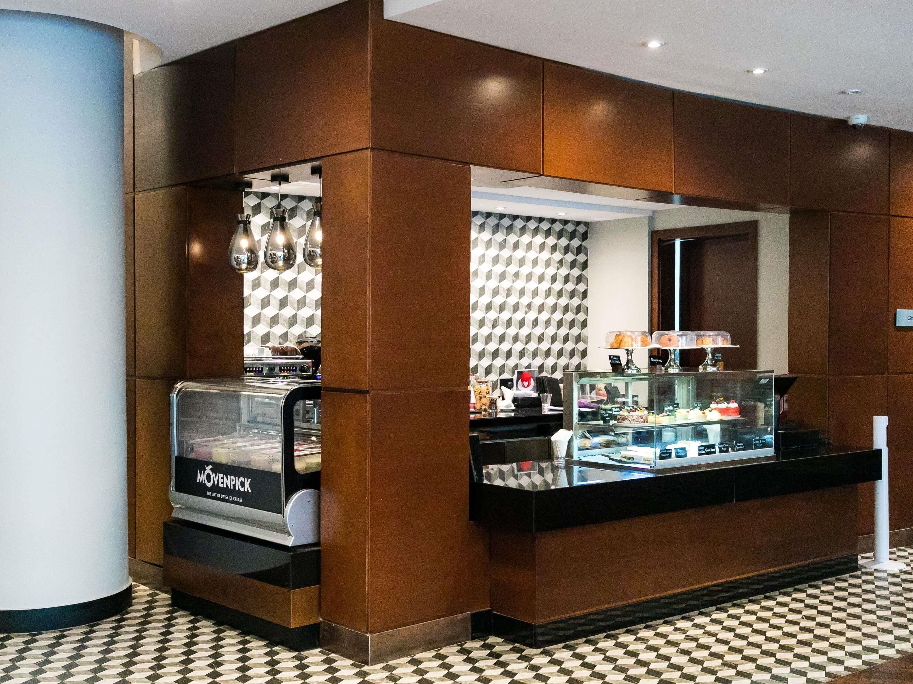 A modern hotel lobby with a coffee station, a glass display case with pastries, and a patterned floor.