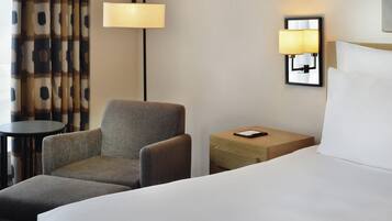 Habitación de hotel con una cama, una silla, una mesita pequeña y dos lámparas fijadas a la pared.