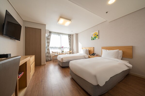 A hotel room with two beds, a desk, a TV, and a window with curtains.
