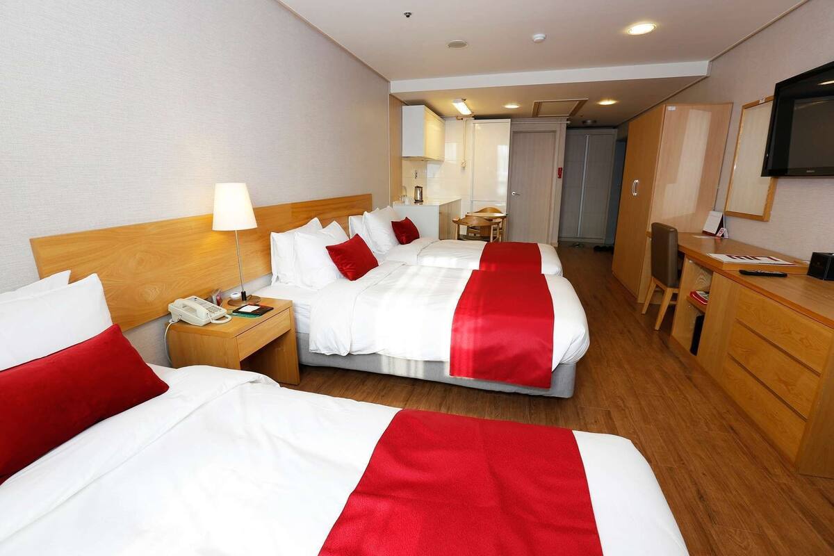 Habitación de hotel con dos camas, un escritorio, una silla, un televisor y un baño a simple vista.