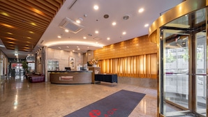 Un hall d'hôtel comprenant un comptoir d'accueil, un espace salon et une entrée en verre.