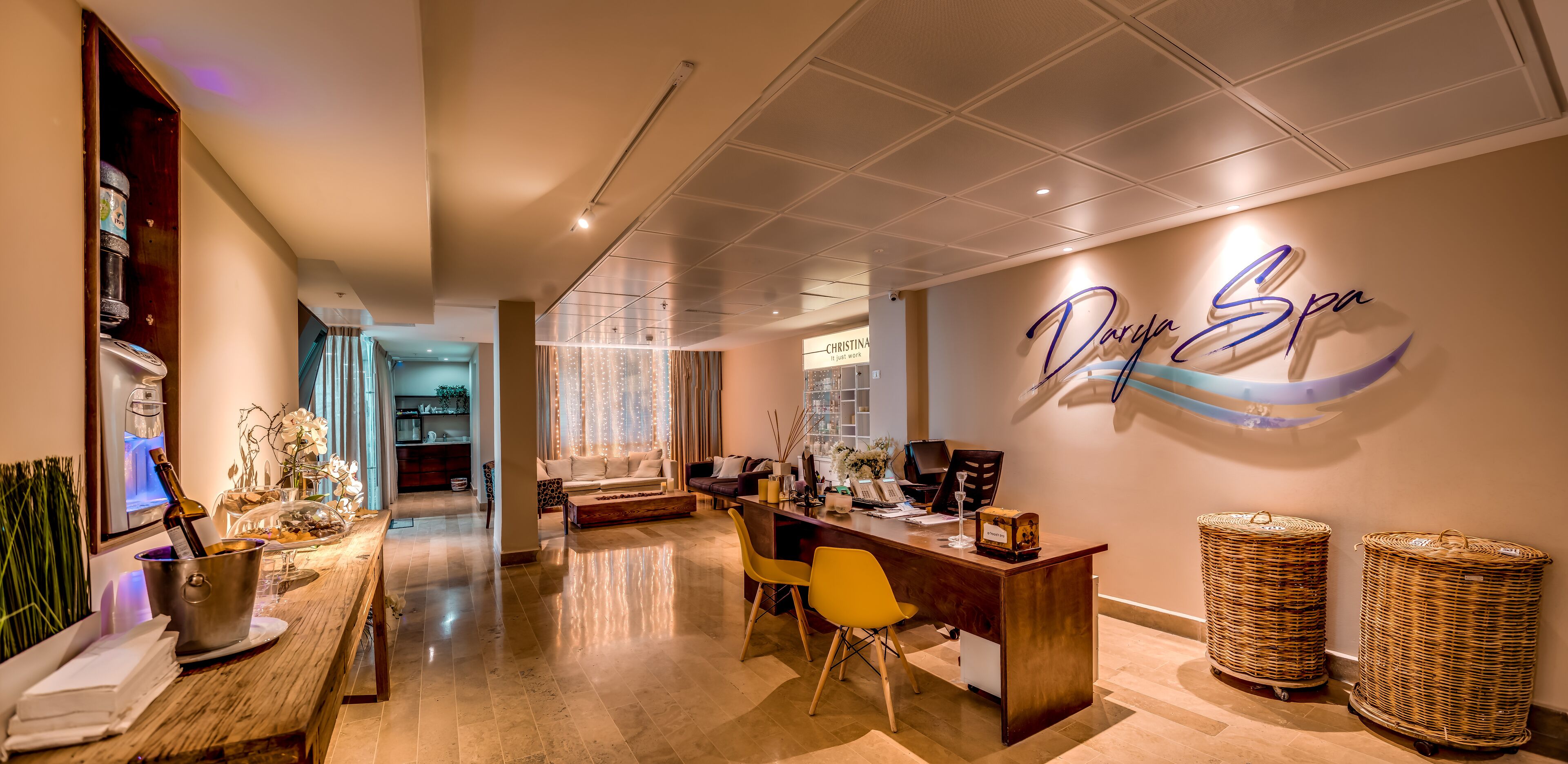 Interior moderno de um spa, com uma mesa de recepção, um grande letreiro na parede com a inscrição "Darja Spa" e uma área de refeições com uma mesa e cadeiras de madeira.