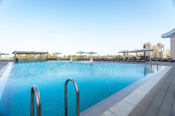 A rooftop pool with clear blue water, surrounded by lounge chairs and umbrellas, with a cityscape in the background. - David's Harp Hotel and Suits (Netanya)