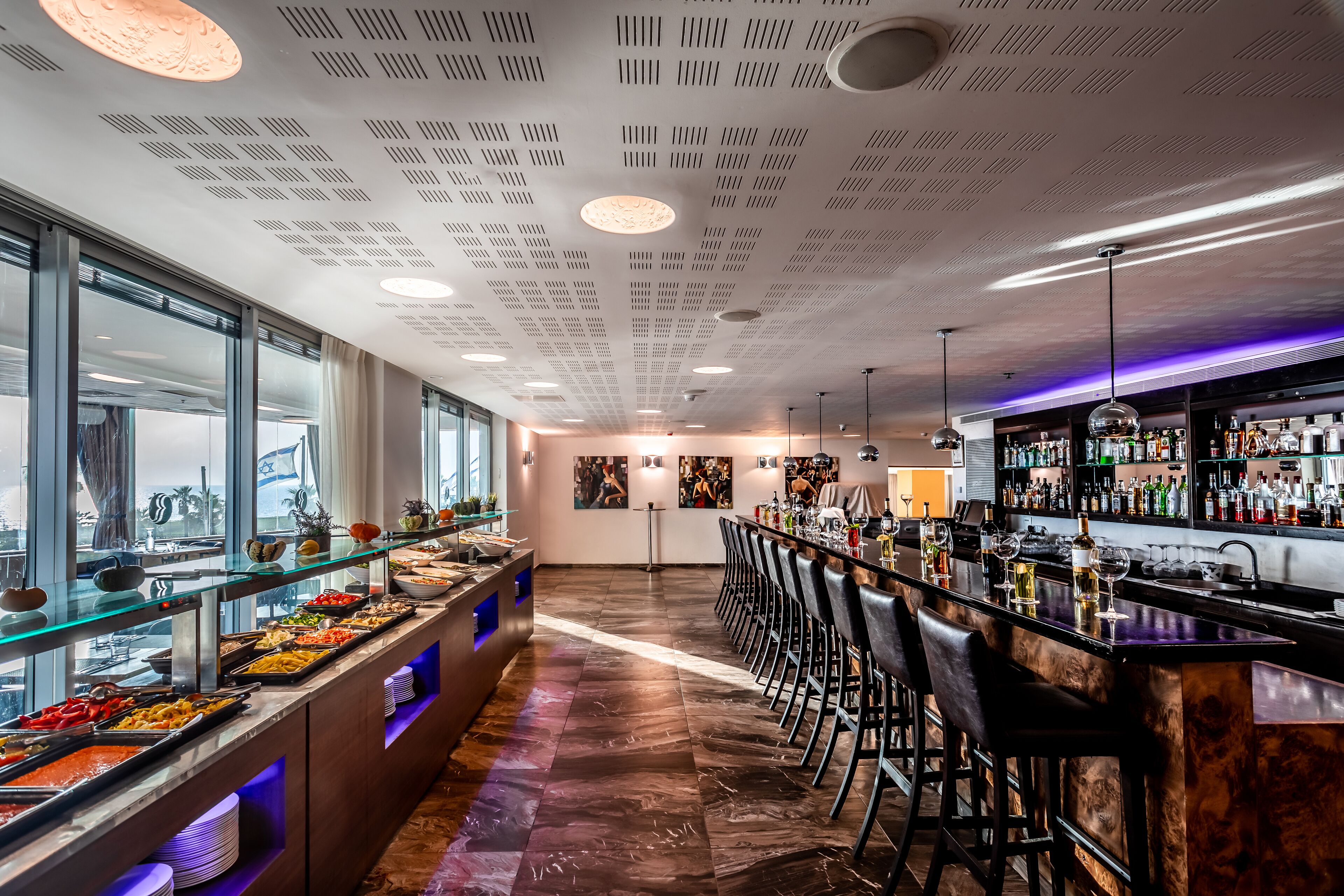 Zona de bar moderna amb una barra llarga, tamborets i una varietat de begudes.