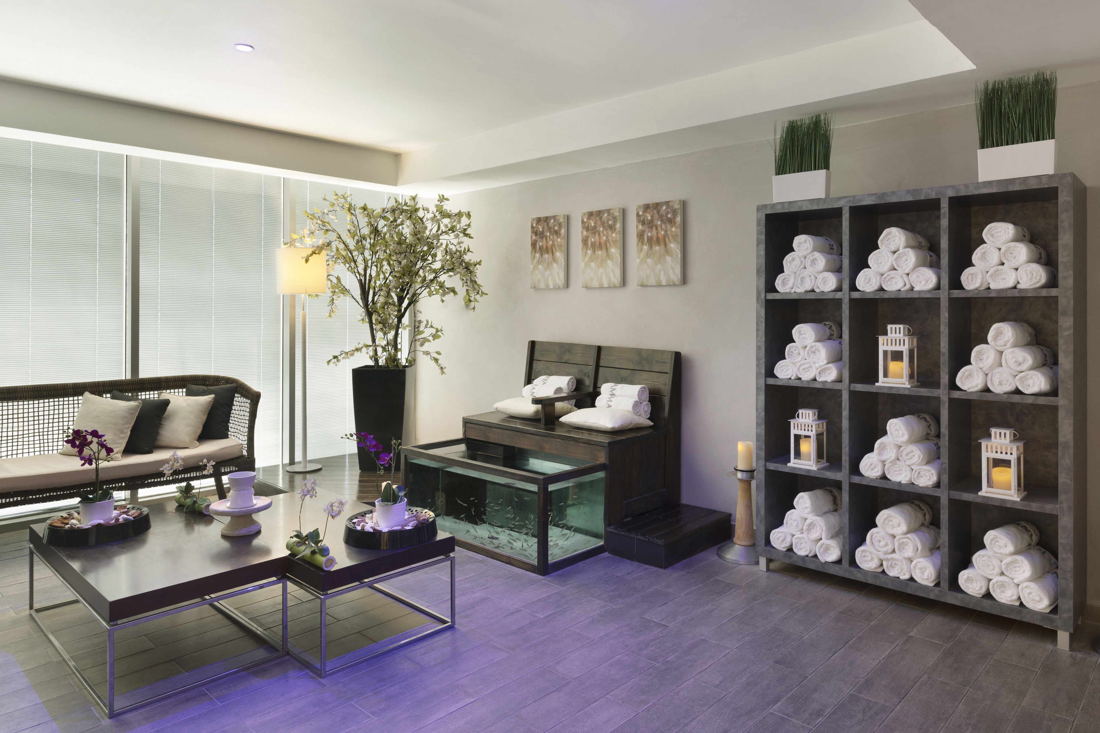 A modern spa room with a glass fish tank, a sofa, a coffee table, and a shelf with towels.