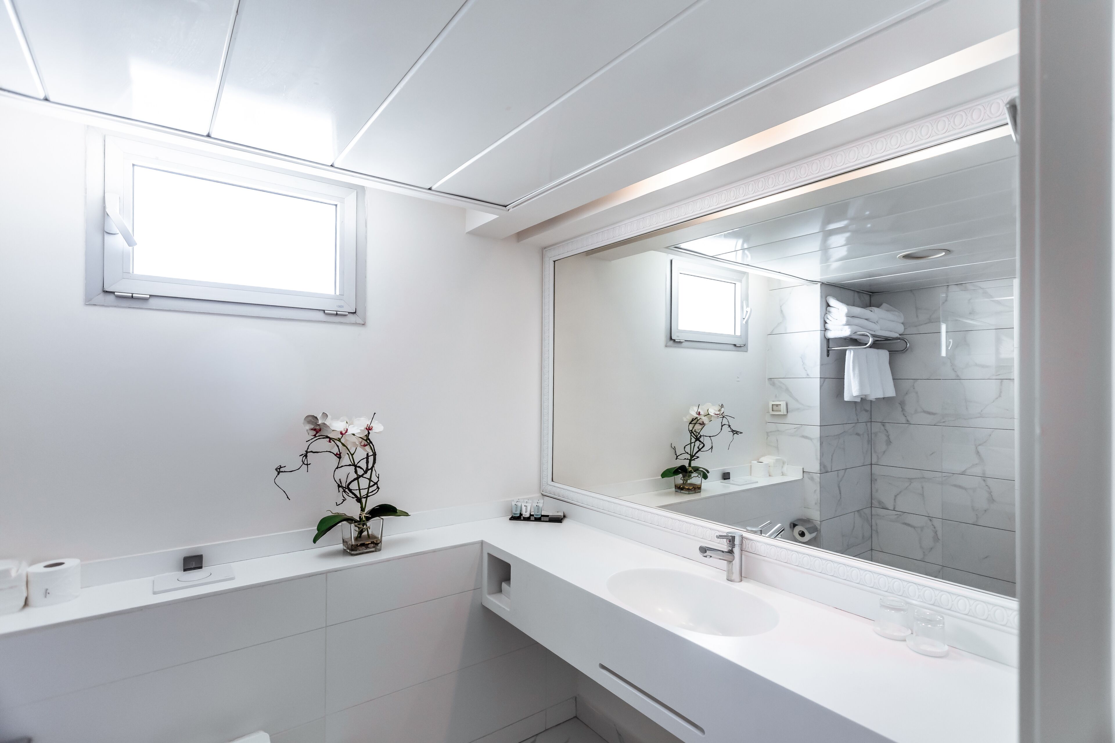A modern bathroom with a large mirror, white fixtures, and a marble backsplash.