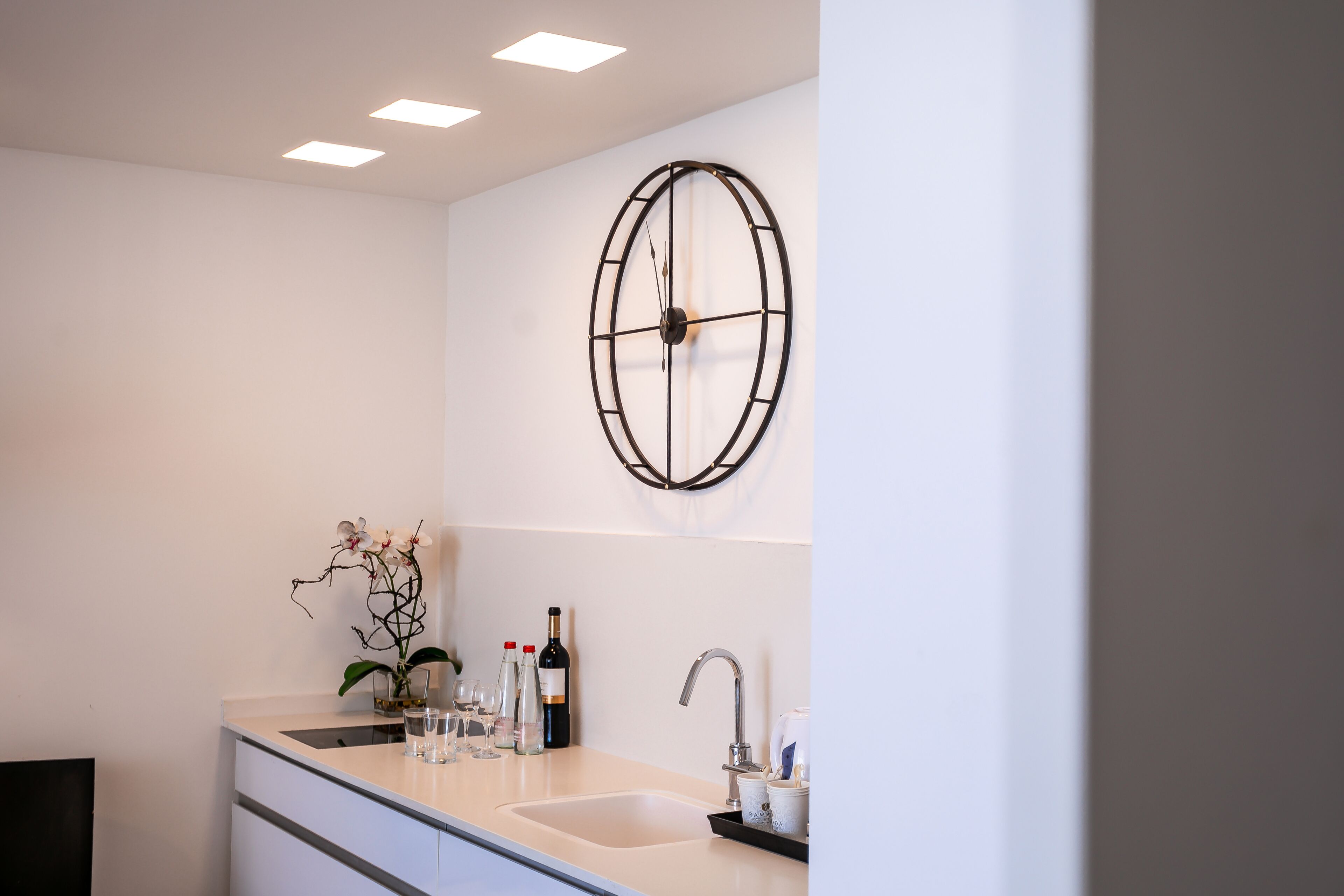 A modern bathroom with a white sink, a decorative metal clock, and a vase of orchids.