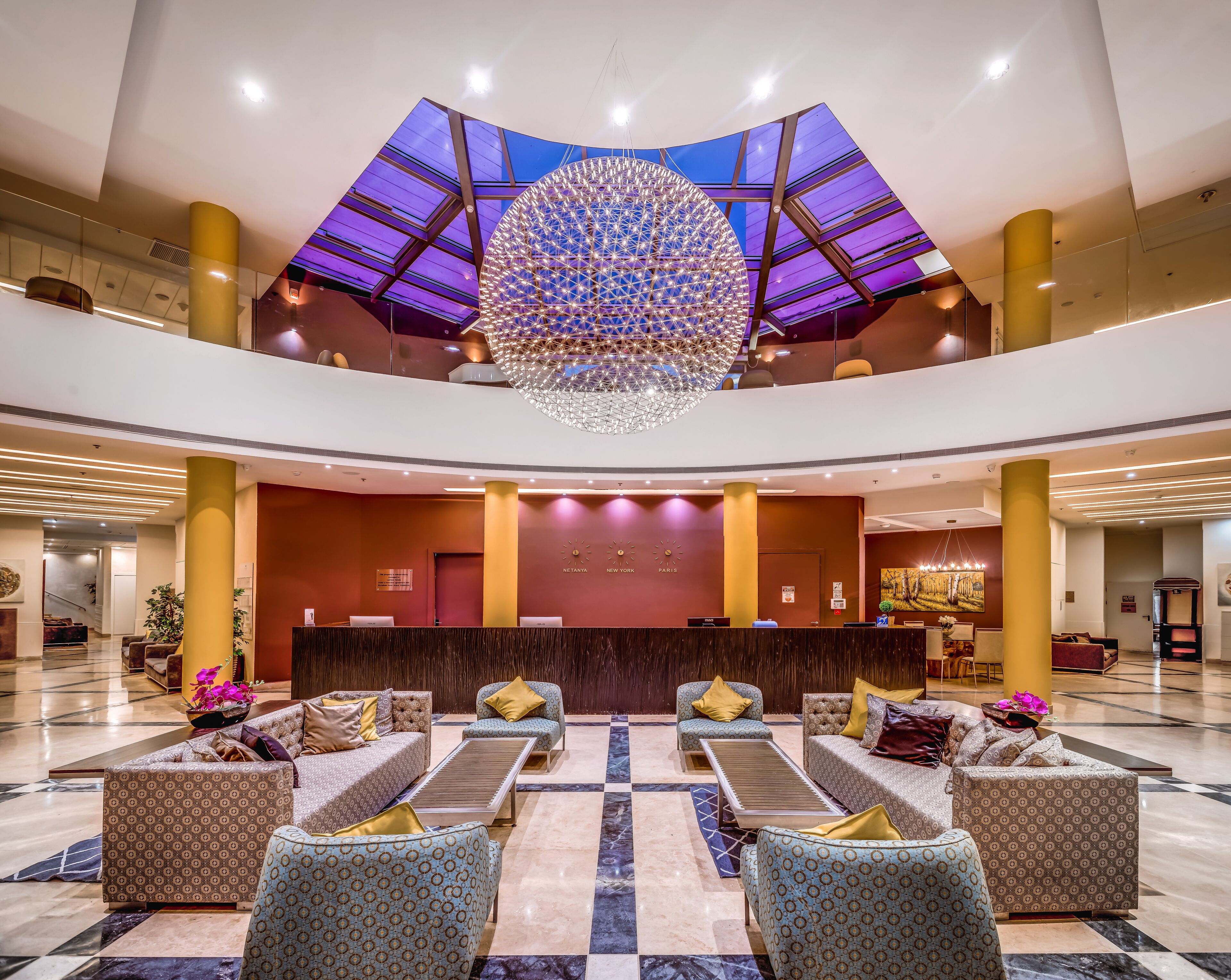 A spacious lobby with a central reception desk, multiple seating areas, and a large decorative chandelier.