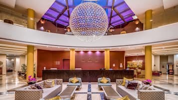 A spacious lobby with a central reception desk, multiple seating areas, and a large decorative chandelier.