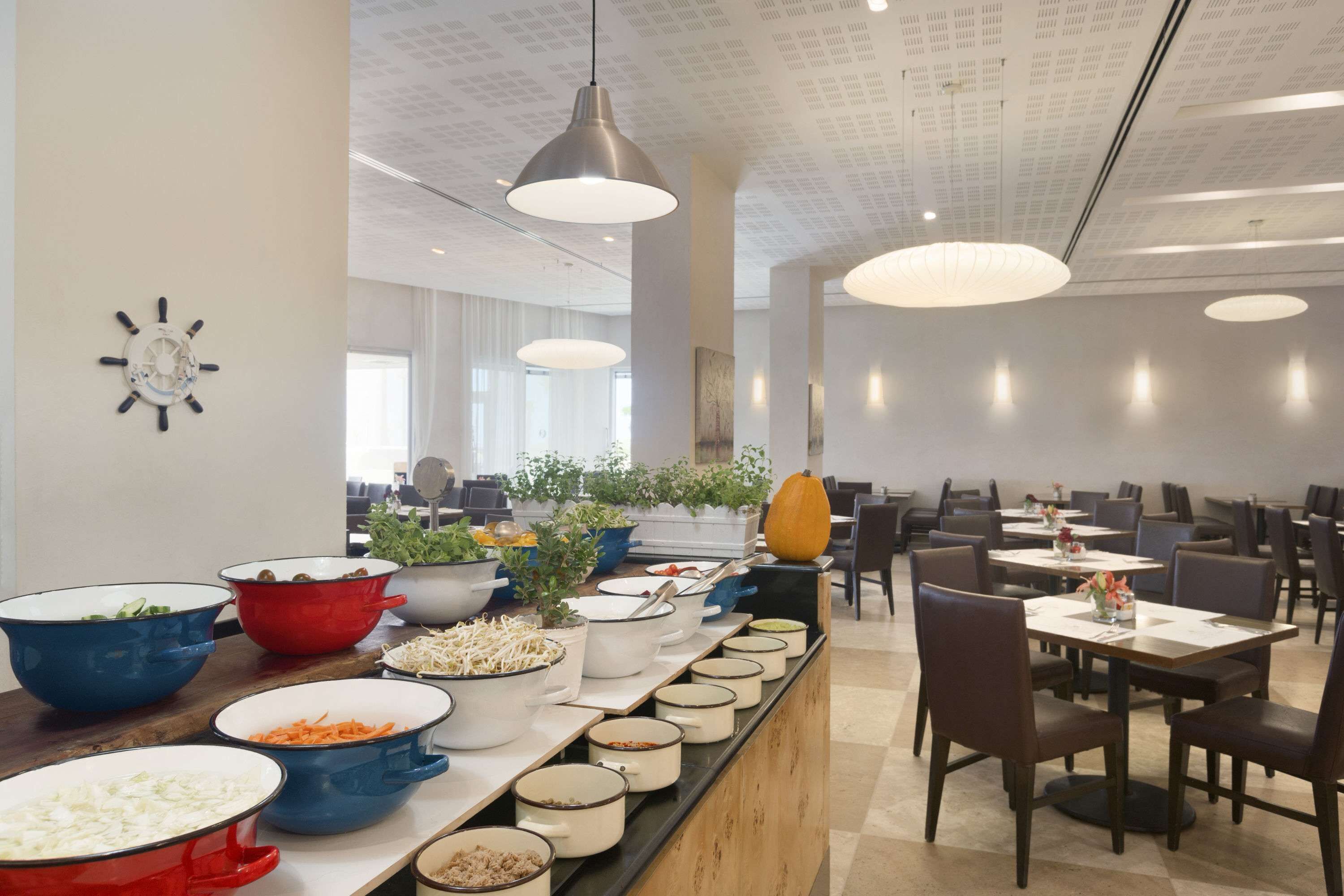 A buffet setup with various dishes and a modern interior with pendant lighting and a clock on the wall.