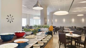 A buffet setup with various dishes and a modern interior with pendant lighting and a clock on the wall.